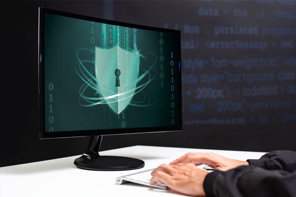 Image of a person and a computer at a desk with the protection logo on the screen