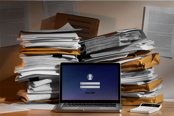 Image of a laptop with many documents and a calculator on the desk